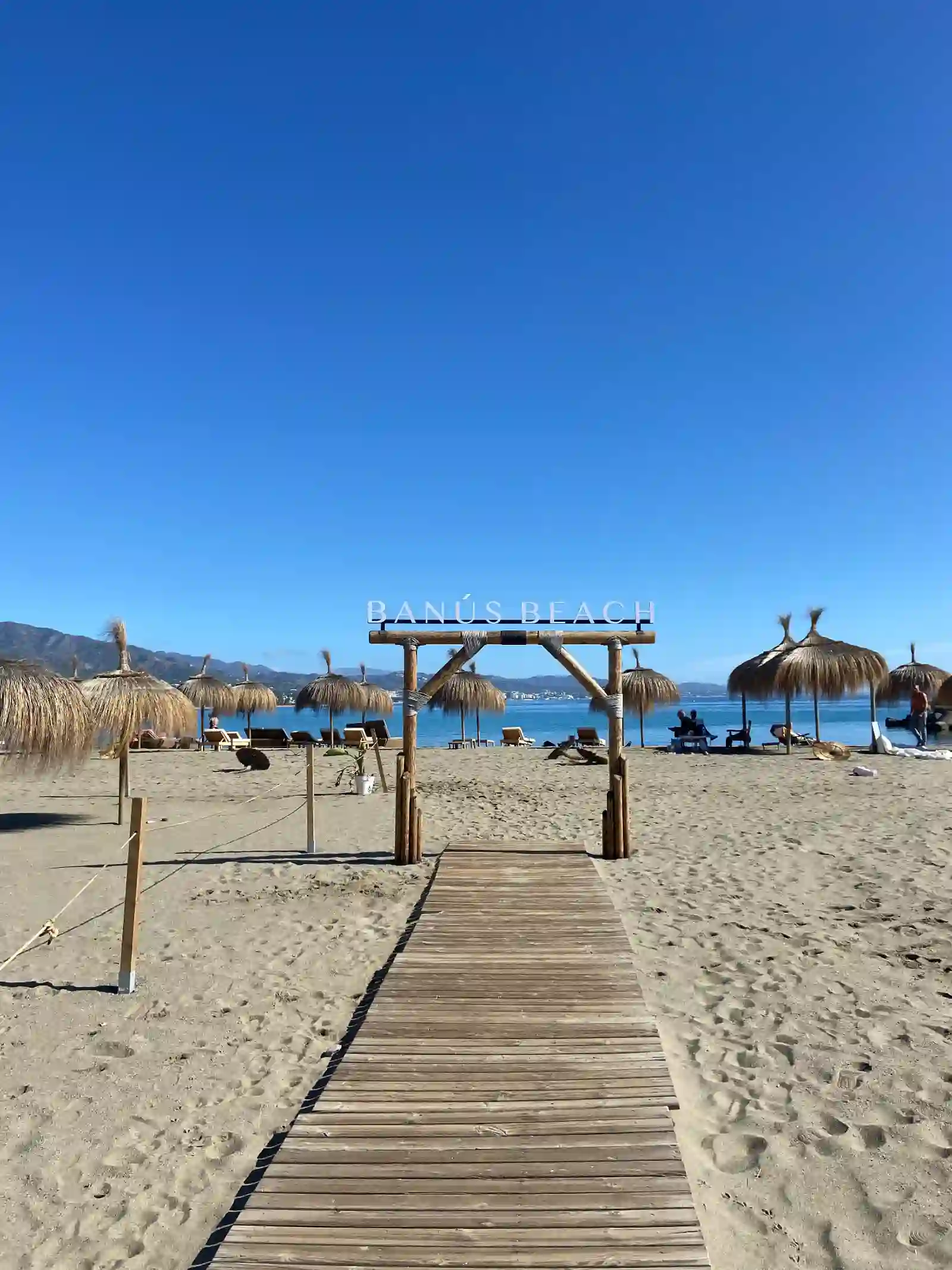 Boardwalk leading onto Playa Puerto Banús with straw parasols, sunbeds and the Mediterranean sea