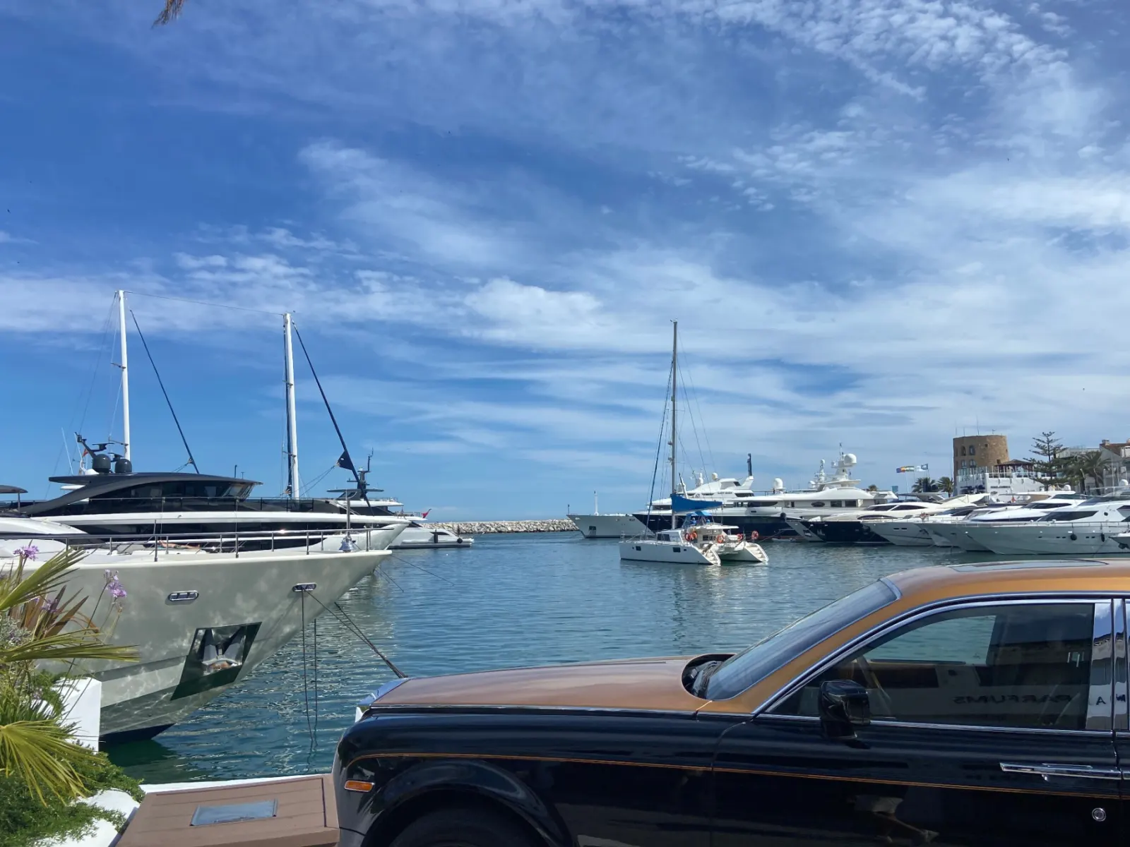 View across Puerto Banús marina with luxury yachts and a Rolls-Royce Phantom in the foreground